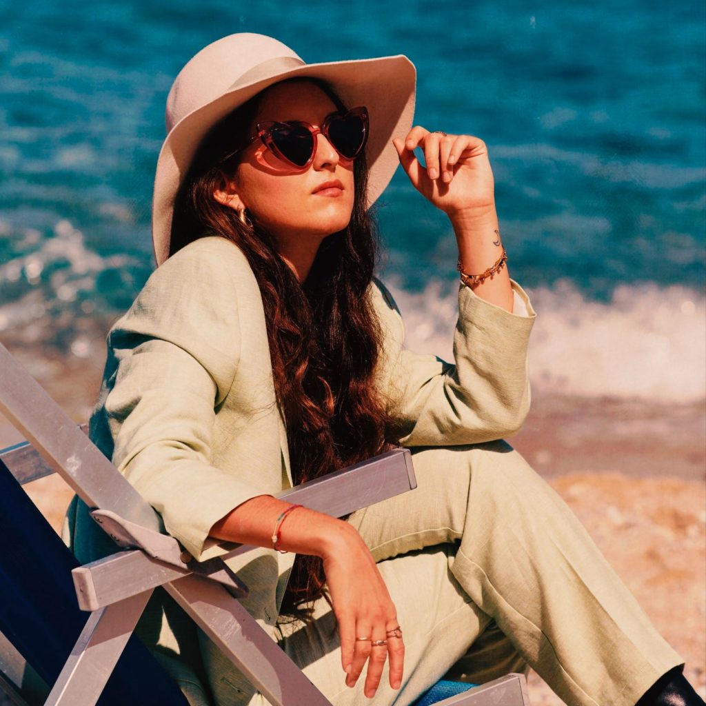 veronica fusaro beach - la cantante seduta in riva al mare su una sedia sdraio, indossa tailleur e cappello chiari e occhiali da sole