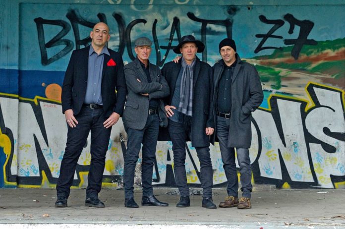 linea fuori mercato - i quattro componenti della band in piedi davanti a un muro disegnato a graffiti