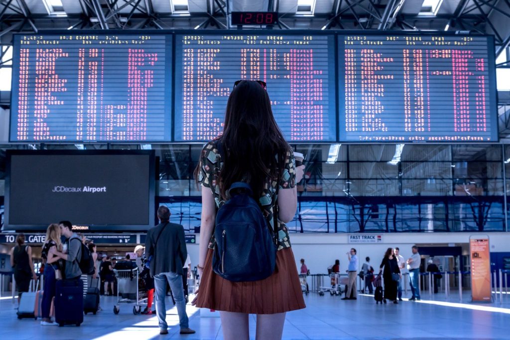 Agenzie di viaggi - una ragazza con lo zaino a spalla davanti al tabellone delle partenze di un aereoporto