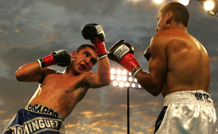 Pugilato, sport, violenza, boxe. Due pugili uno davanti all'altro. Sulla sinistra l'atleta sta ricevendo un pugno e si copre il viso con il braccio.