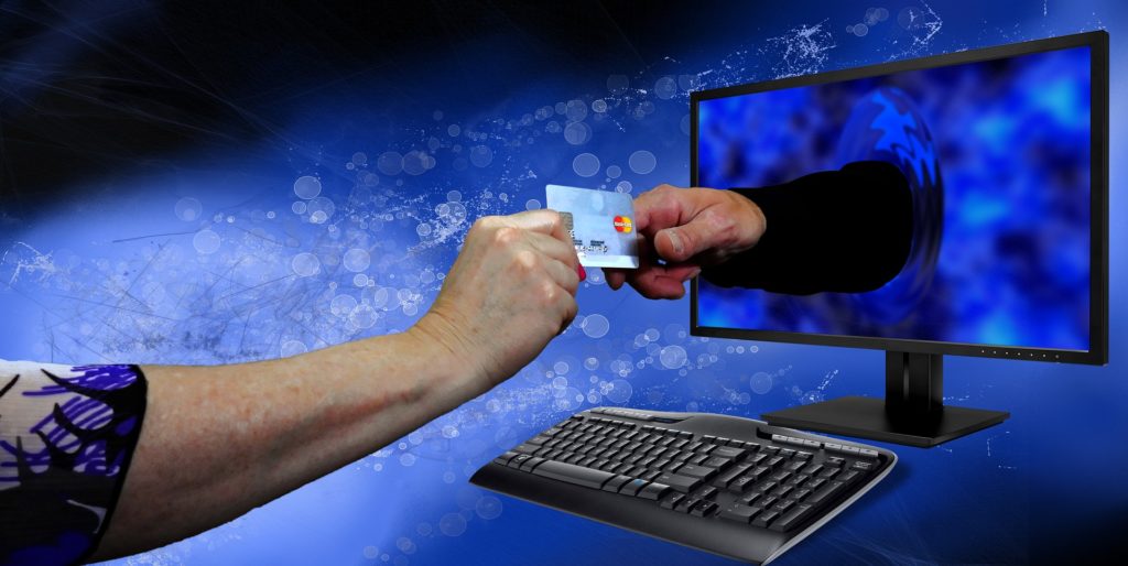 promozioni e saldi - una mano sporge una carta di credito ad un'altra mano che esce dallo schermo di un computer