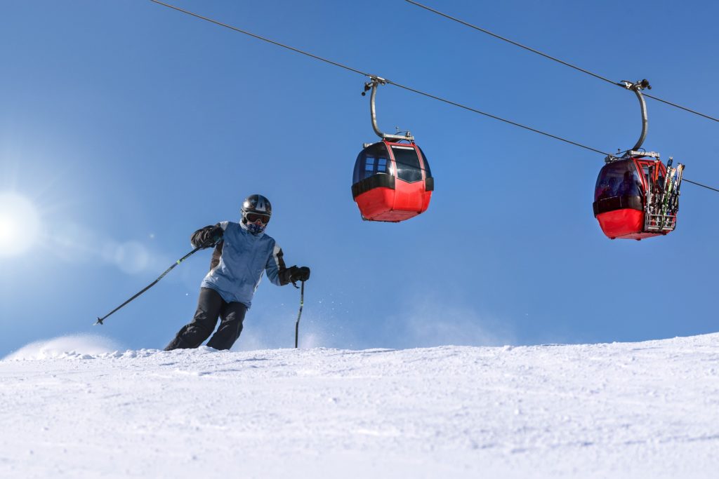 agenzie di viaggi - uno sciatore su una pista da sci e sopra di lui le cabine di una funivia