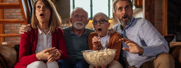 Il Natale sta arrivando - una famiglia composta da mamma papà nonno e nonna seduti su un divano con in brccio una grande terrina di popcorn gurdano meravigliati la tv
