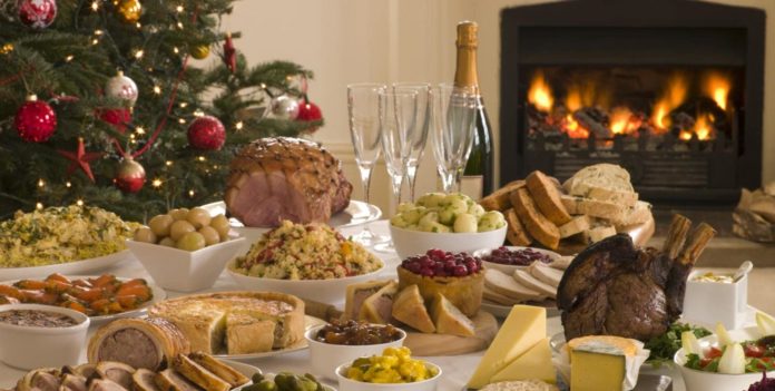 pranzo di natale con tanti piatti pieni di cibo e sulo sfondo un caminetto acceso e un albero di natale illuminato