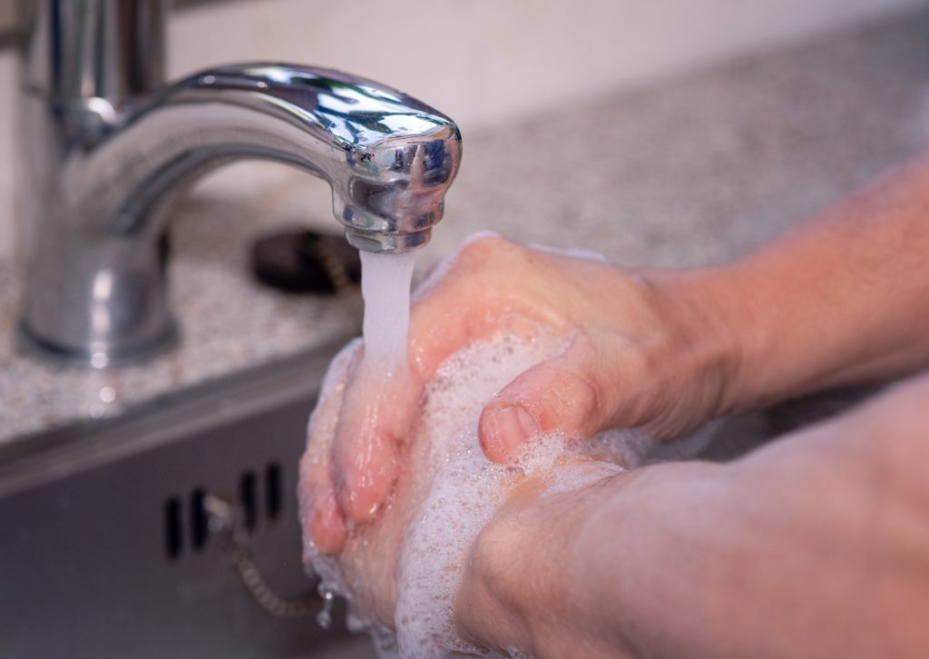 una persona si stalavando le mani con sapone sotto l'acqua di un lavandino