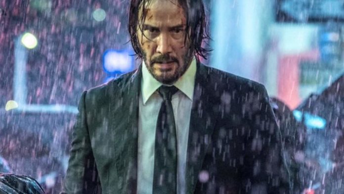 John Wick (Keanu Reeves) con giacca e cravatta sotto la pioggia.