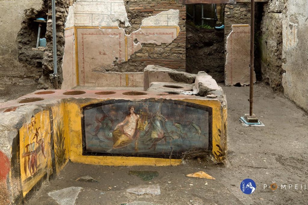 streetfood e lounge bar a pompei, un bancone di pietra con affreschi sui lati e dei recipienti scavati nella pietra del bancone