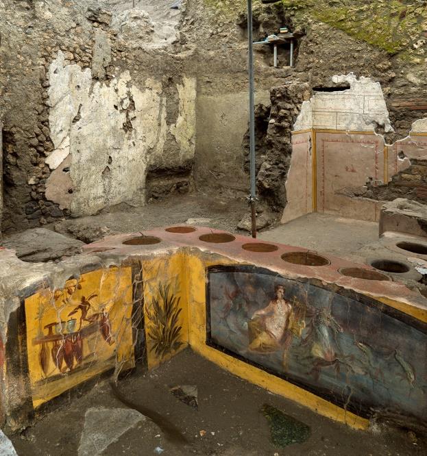 un bancone di pietra con affreschi sui lati e dei recipienti scavati nella pietra del bancone