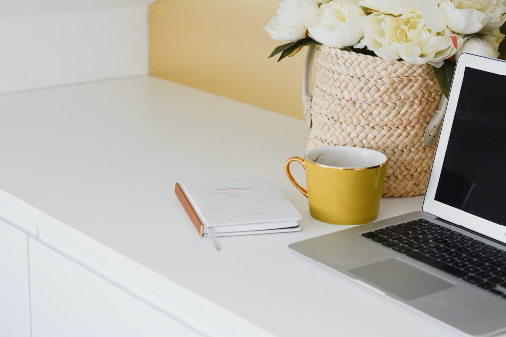 casa idee studio tortora - un ripiano con sopra un laptop, una tazza gialla, un quaderno e un vaso di vimini con dentro dei tulipani bianchi