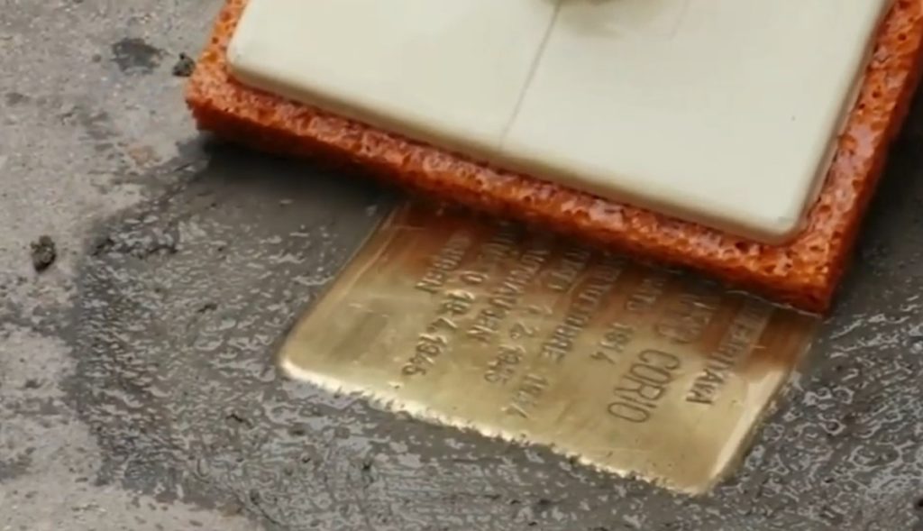 Giorno della memoria pietre d'inciampo shoah - la posa di un sanpietrino con la targa dorata che riporta il nome della vittima dell olocausto, il luogo dove abitava e la data della deportazione con un pennello spugna che la incastra nel pavimento della strada