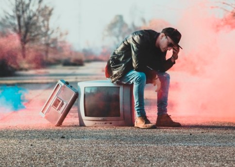 addio - grace n kaos - la copertina del disco con un ragazzo con cappellino, jeans e giubbotto nero, seduto su un televisore con una radio appoggiata di sbieco. il tutto è in mezzo a una strada e intorno a lui del fumo rosa e azzurro