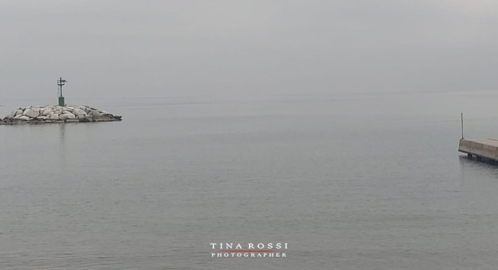 Liguria - nebbia sul mare e ai lati un piccolo isolotto e dall'altra parte il fondo di un molo del porto