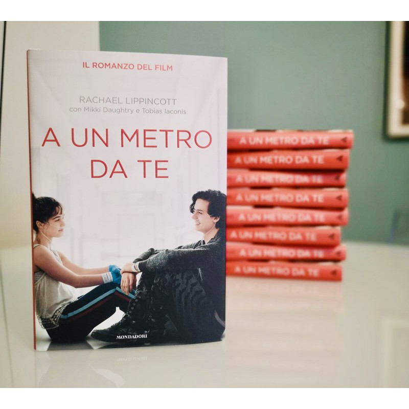 A un metro da te, romanzo, amore. Sulla copertina del libro sono presenti i due protagonisti, uno difronte all'altro, mentre sorridono. Dietro il libro, appoggiato su un piano, sono presenti altre copie una sopra l'altra.