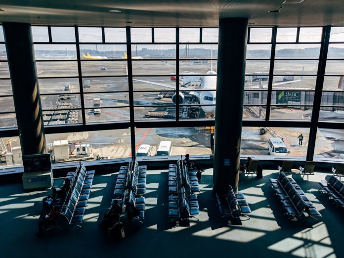 Viaggiare oggi - nella foto la sala d'attesa di un aeroporto cn tante sedie e un'enorme vetrata da cui si vede un aereo parcheggiato e diversi veicoli