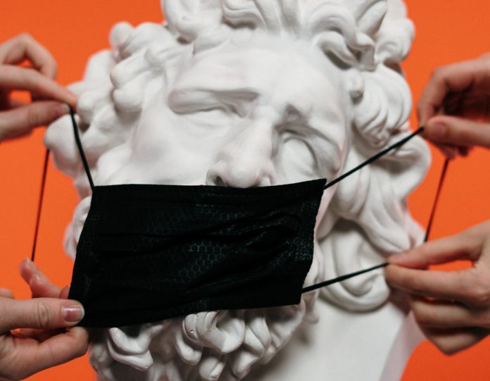 L'Italia al tempo del Covid - la tsta di una statua greca con delle mani che gli mettono una mascherina
