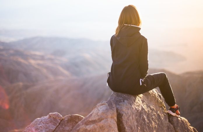 Una donna seduta di spalle su una roccia in alto su una montagna guarda il panorama