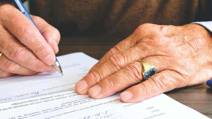 nella foto si vedono le mani di uomo con un vostoso anello d'oro con pietra quadrata blu, che sta firmando un foglio