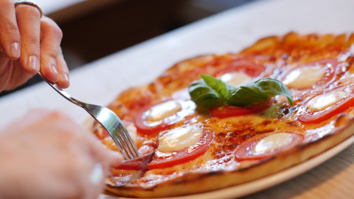 Ristoranti aperti di sera - nella foto una persona sta mangaindo una bella pizza in primo piano con coltello e forchetta