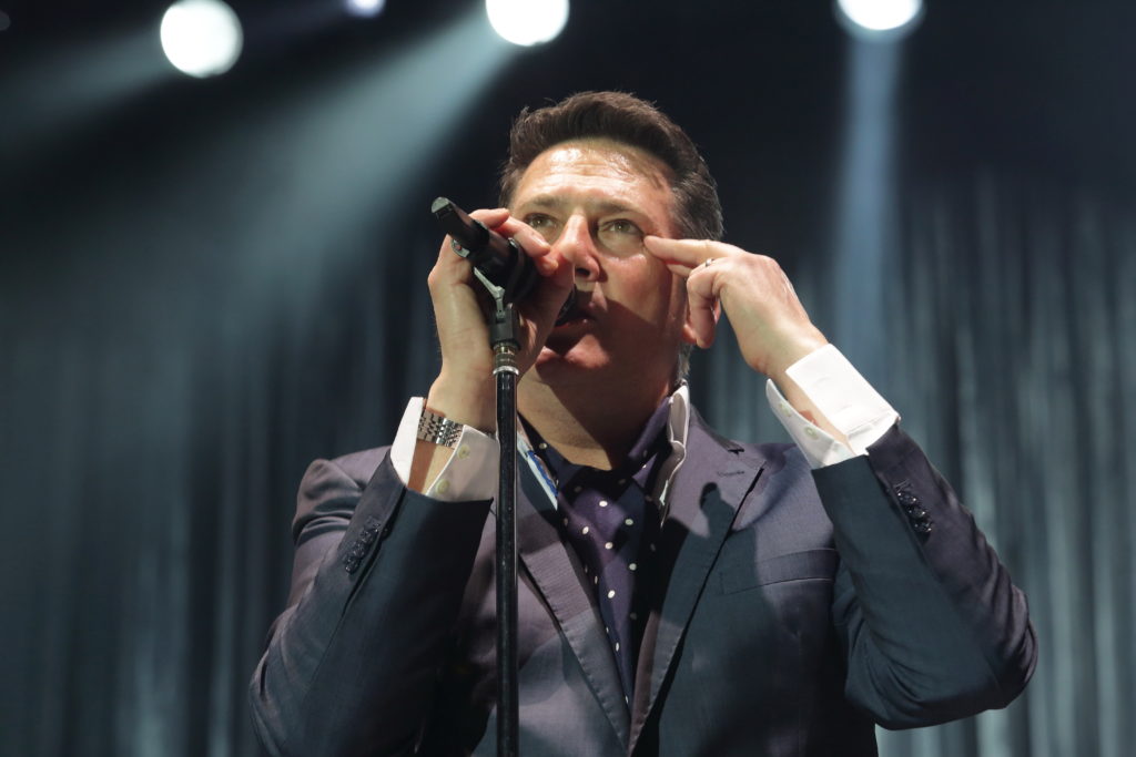 tony Hadley, vestito grigio a camicia bianca, col microfono nella mano destra, la mano sinistra che tocca la tempia