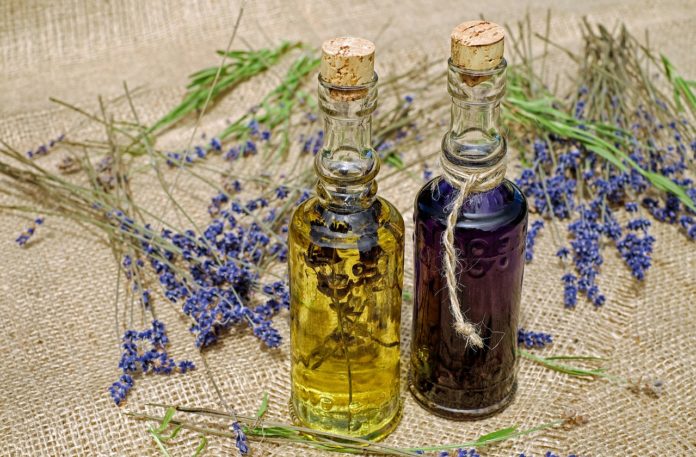 Lavanda proprietà e benefici - nella foto, su un tavolo di legno dei rametti di lavanda viola e due boccettte da erborista, in un a del liquido giallo, nell'altra del liquido scuro