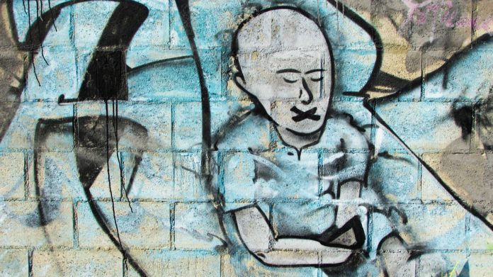 Un murales a sfondo azzurro con un uomo calvo con gli occhi chiusi e la bocca a forma di 