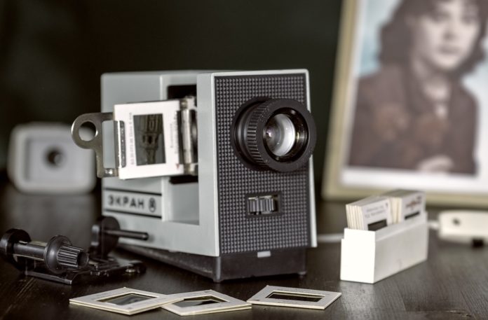 speciale scuole una vecchia cinepresa in primo piano e sullo sfondo sfocato una cornice con una fotografia in bianco e nero di una donna. Davanti alla cinepresa delle diapositive