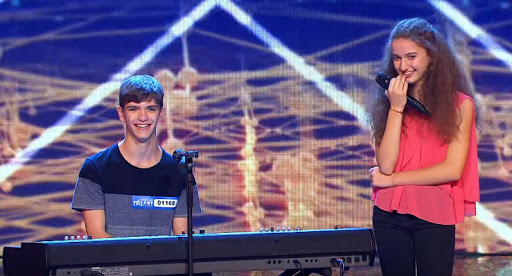 in foto da sinistra Francesco Faggi al piano, a destra Elena Faggi col microfono in mano, sorridono davanti ai giudici di Italia's got talent, sullo sfondo lo studio televisivo, Francesco indossa una t-shirt a righe blu scuro e grigio, Elena ha una camicia rosa smanicava e un jeans nero