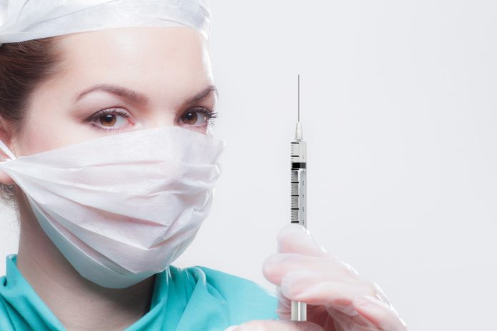 Vaccini - una donna infermiera con mascherina bianca e camice verde tiene in mano una siringa