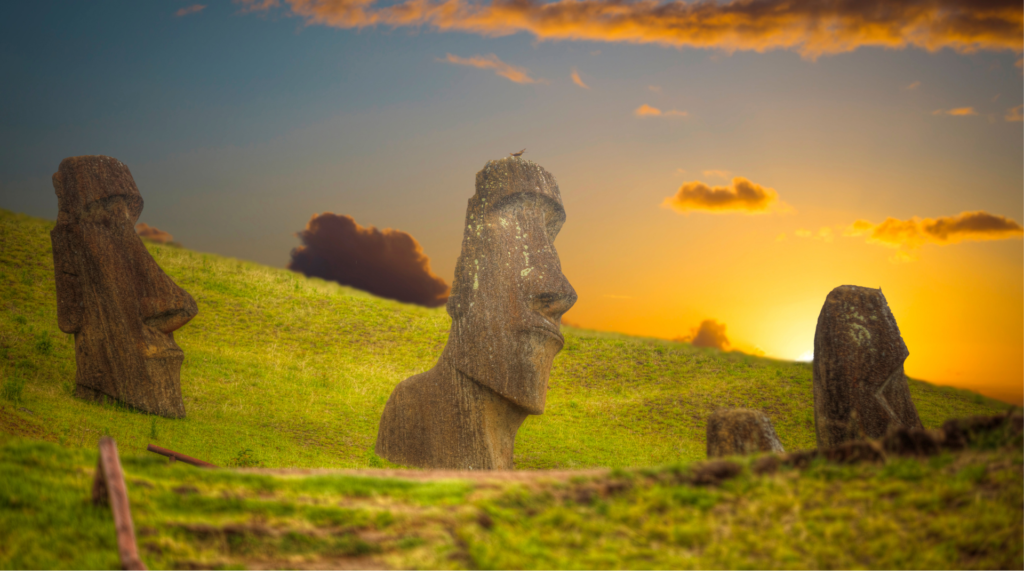 Le famose statue di teste di pietra piantate sul versante di una collina verde. Il cielo è un tramnto arancione