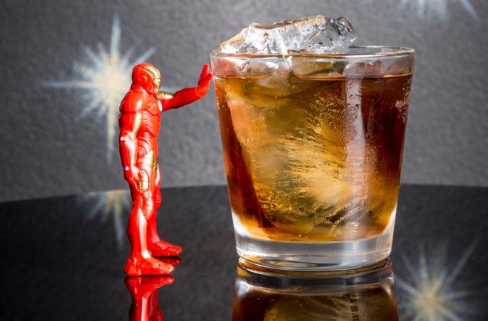 Iron Man la statuita, con il braccio tocca un bicchiere pieno di ghiaccio e di uncocktail che si chiama demon in a bottle