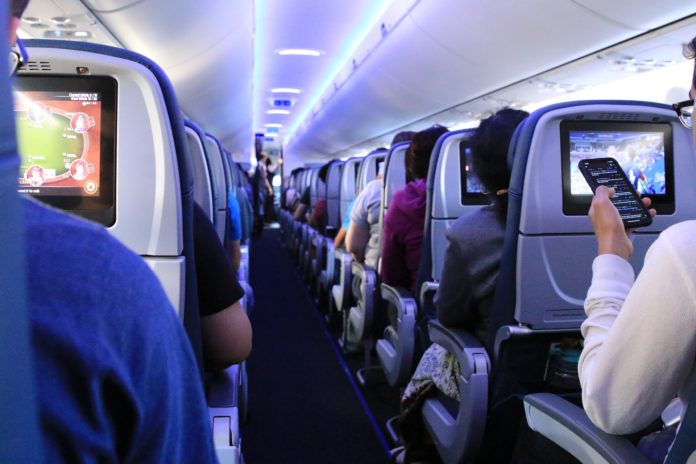 Malpensa voli covid-tested - l'interno di un aereo pieno di passeggeri seduti mentre guardano sul monitor posizionato sullo schienale, una signora, di schiena sta guardando il suo cellulare