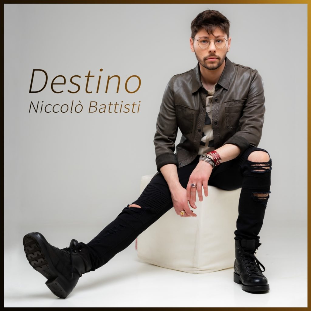 sesdtino - la copertina del singolo che vede niccolò battisti seduto su uno sgabello bianco, jeans neri con gli strappi e camicia lucida marrone