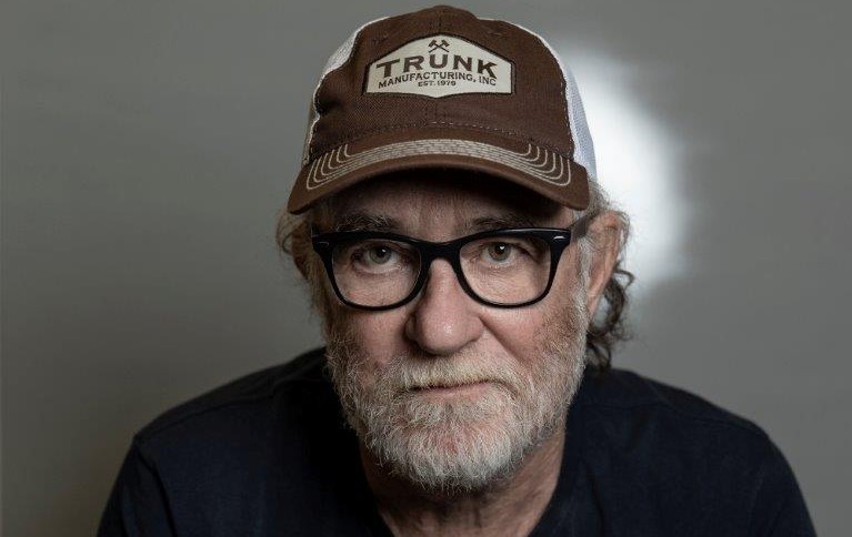 Francesco DE GRegori nella foto in primo pano, serio, con barba bianca, caèpellino beoge, t shirt nera