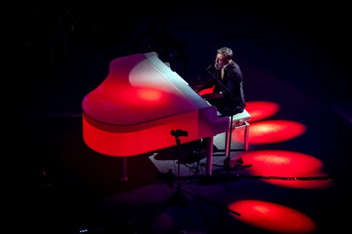 Marco Masini seduto al pianoforte illuminato da dei fari rossi