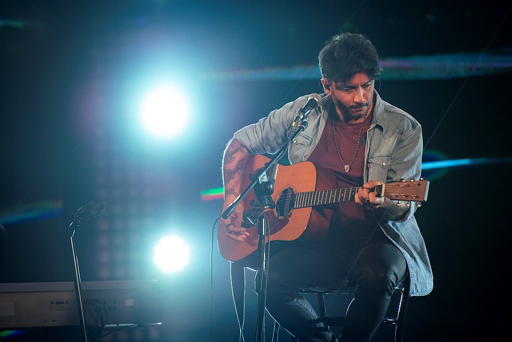 tour di Fabrizio Moro canta seduto su uno sgabello e suona la chitarra