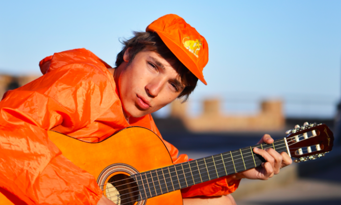 Zo Vivaldi, in foto ha un cappello arancione, è vestito di arancione, tiene in mano una chitarra