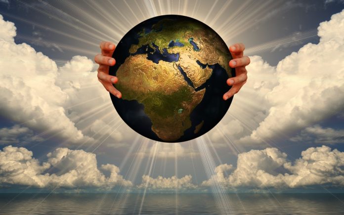 Un globo rappresentante la Terra nella mani di un uomo . Il globo è nel cielo irradia raggi di luce e intorno, delle nuvole e, sotto, il mare