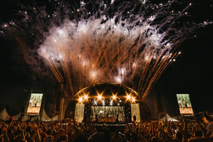 Musicultura Festival 2021 - Un concerto live di musica con tantissima gente e un palco illuminato con riflettori arancioni. Nel cielo esplodono fuochi d'artificio
