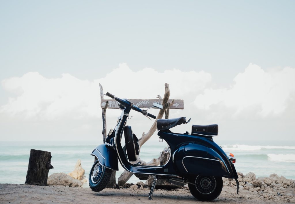 anni 60 .una vespa blu parcheggiata davanti alla spiaggia, sullo sfondo il mare