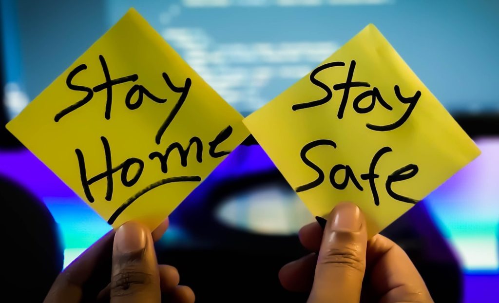 Pandemic Fatigue - in primo piano due post it con la scritta "stay home" e "stay safe" tenuti da due dita e sullo sfondo un o schermo di pc