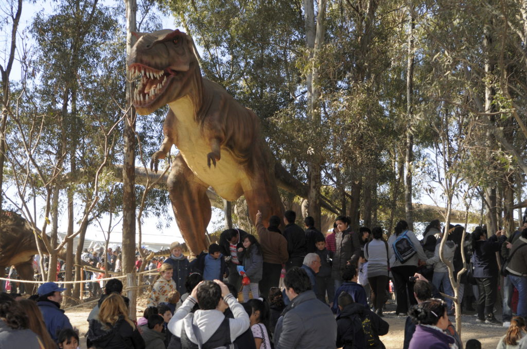 t-rex a grandezza naturale con grandi denti aguzzi e un'espressione feroce. Sotto di lui diversi visitatori del parco, con bambini e adulti
