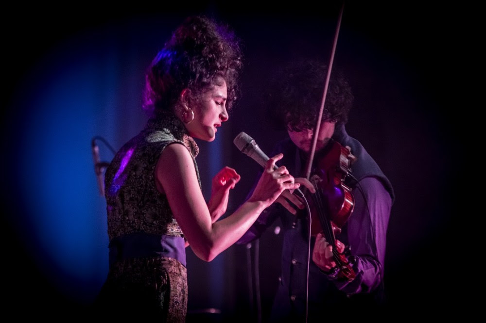 Still Life nella foto la cantante con capelli raccolti indossa una canottiera viola, è di profilo e canta sul palco illuminata da una luce viola, vicino a lei un altro componente della band suona il violino