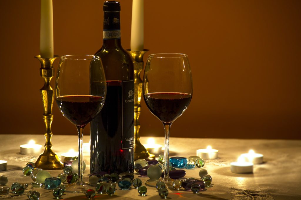 social e food porn - due bicchieri riempiti a metà con del vino rosso, sonoposizionati ai lati di una bottiglia di vino rosso, sono appoggiati su una tavola su cui ci sono sparse delle stelline bianche e delle pietre trasparenti colorate