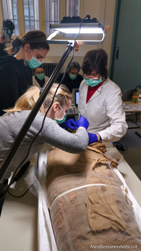 degli scienziati con camice bianco operano un restauro su un amummia egizia