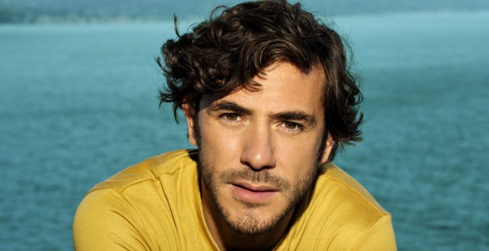 jack savoretti in primo piano ha la maglia gialla, dietro il mare