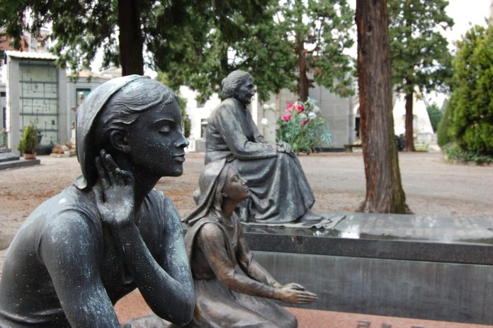 Monumentale di Milano: due statue di marmo raffiguranti una donna giovane e una vecchia, su due tombe in mezzo ad un prato del cimitero