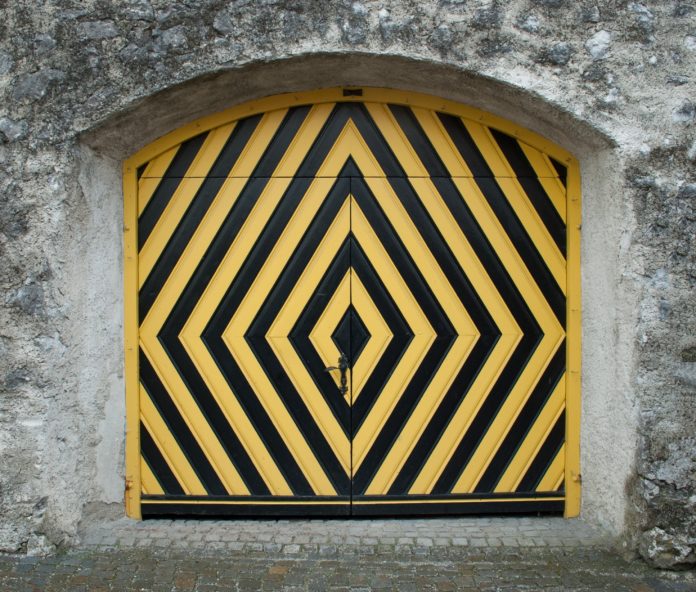 progetto editoriale - un portone di legno pitturato con strisce gialle e nere diagonali, a formare dei rombi, il portone è fissato in una parete di pietra