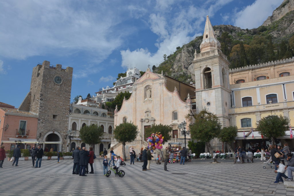 Taormina, la piazza con la chiesa con il campanile e molta gente a passeggio