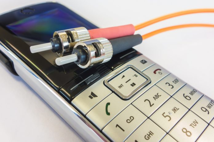 due cavi di fibra ottica, uno con spinotto rosso e l'altro con spinotto nero, appoggiati su Un telefonino color argento con display azzurro