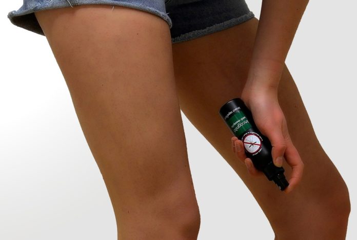 nella foto si vedono due gambe di donna che insdossa un pantaloncino di jeans corto, nell'atto di spruzzasi con un abomboletta spray un repellente per zanzare